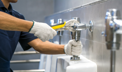A plumber is using a wrench to fix or repair leaking water pipes, faucets or valves in toilet bowls and sinks in restroom