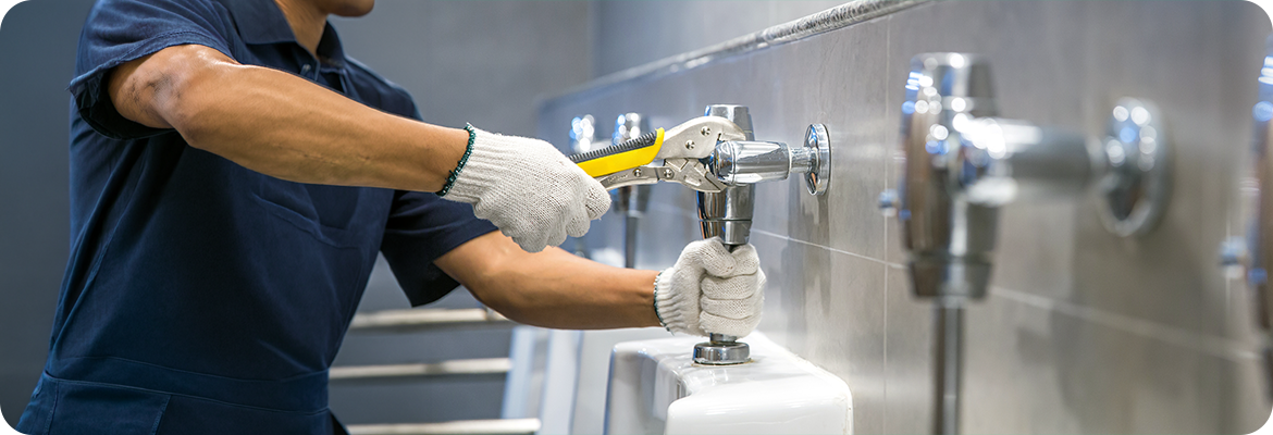 A plumber is using a wrench to fix or repair leaking water pipes, faucets or valves in toilet bowls and sinks in restroom